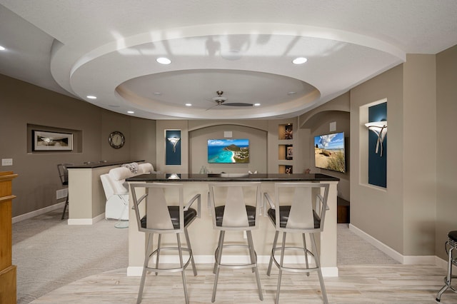 bar featuring light carpet, ceiling fan, and a tray ceiling