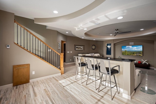 bar with ceiling fan, a tray ceiling, and light hardwood / wood-style flooring