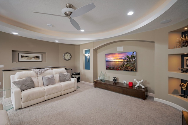 living room featuring light carpet, a tray ceiling, built in features, and ceiling fan