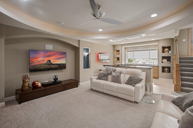 living room with ceiling fan, a raised ceiling, light carpet, and a textured ceiling