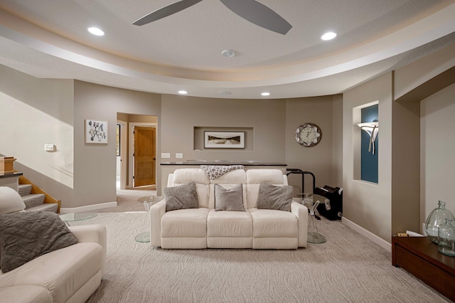 living room featuring a raised ceiling, light carpet, and ceiling fan