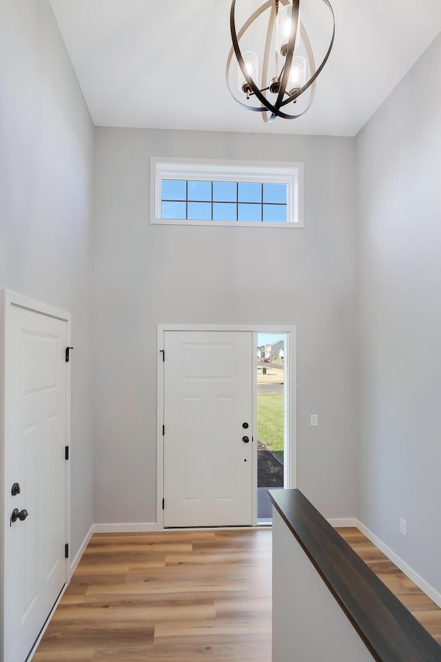 foyer with an inviting chandelier, a towering ceiling, plenty of natural light, and light hardwood / wood-style floors