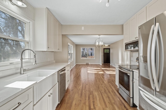 kitchen featuring stainless steel appliances, a notable chandelier, white cabinets, decorative light fixtures, and light wood-type flooring