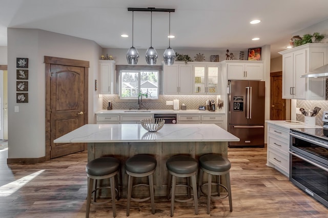 kitchen featuring a kitchen island, appliances with stainless steel finishes, decorative light fixtures, white cabinetry, and light stone counters