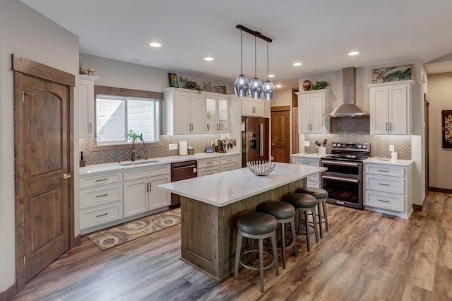 kitchen with white cabinetry, sink, a center island, stainless steel appliances, and wall chimney exhaust hood