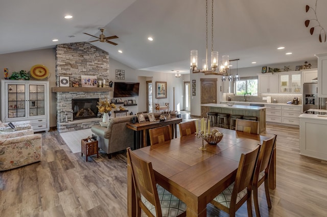 dining room featuring a stone fireplace, vaulted ceiling, light hardwood / wood-style floors, and ceiling fan