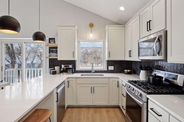 kitchen featuring pendant lighting, sink, lofted ceiling, white cabinetry, and stainless steel appliances