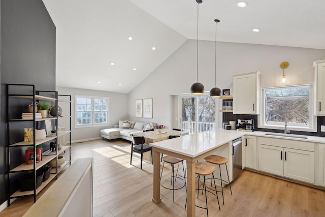 kitchen featuring sink, light hardwood / wood-style floors, decorative light fixtures, stainless steel dishwasher, and kitchen peninsula