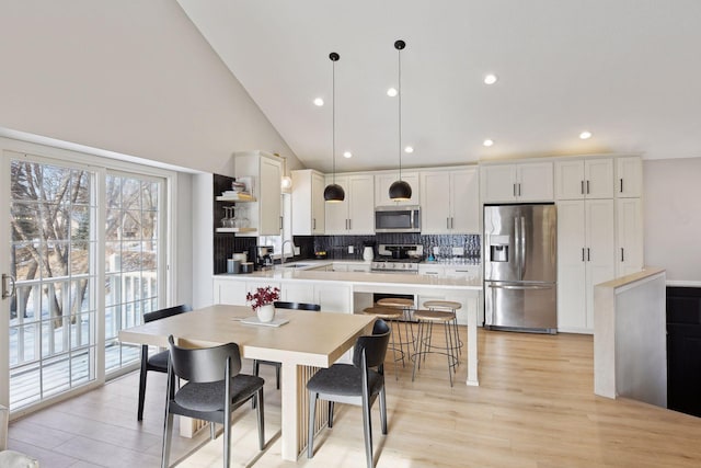 kitchen with tasteful backsplash, hanging light fixtures, light wood-type flooring, appliances with stainless steel finishes, and white cabinets