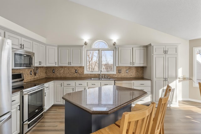 kitchen with sink, appliances with stainless steel finishes, white cabinets, a kitchen island, and vaulted ceiling