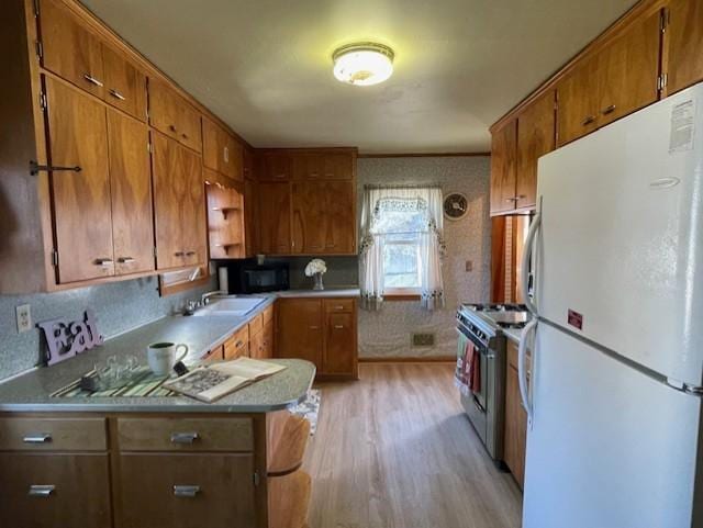 kitchen with brown cabinets, freestanding refrigerator, stainless steel gas stove, light wood-type flooring, and black microwave