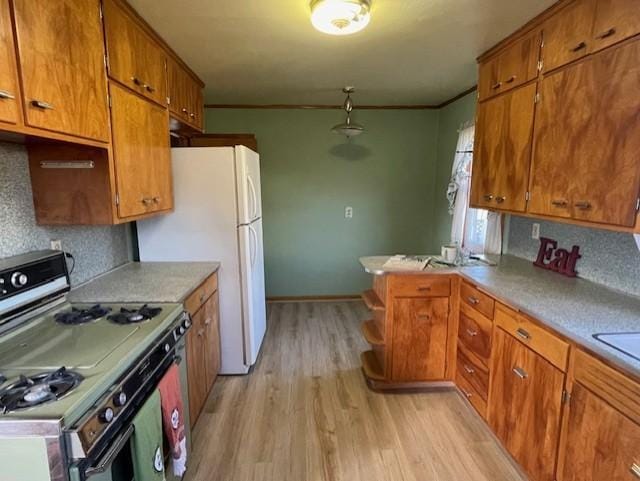 kitchen featuring light wood finished floors, brown cabinetry, gas range oven, light countertops, and crown molding