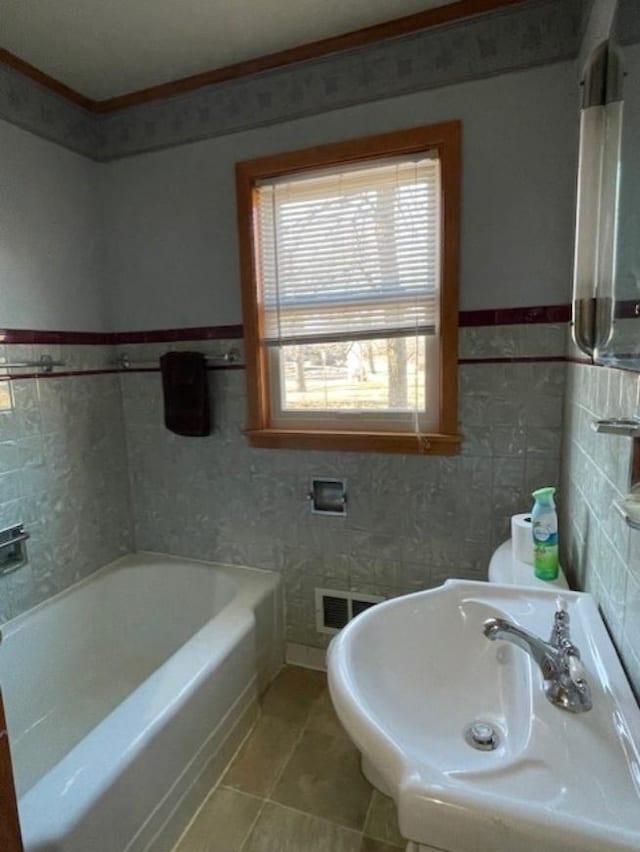 full bath with a tub to relax in, a sink, tile walls, visible vents, and tile patterned floors