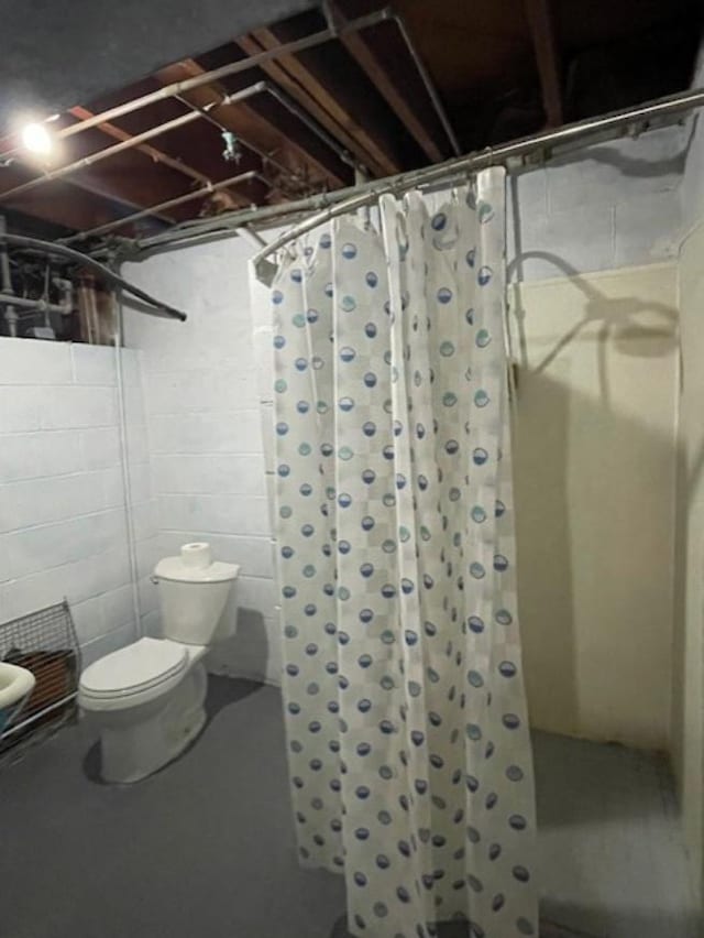 bathroom with concrete flooring, a stall shower, and toilet