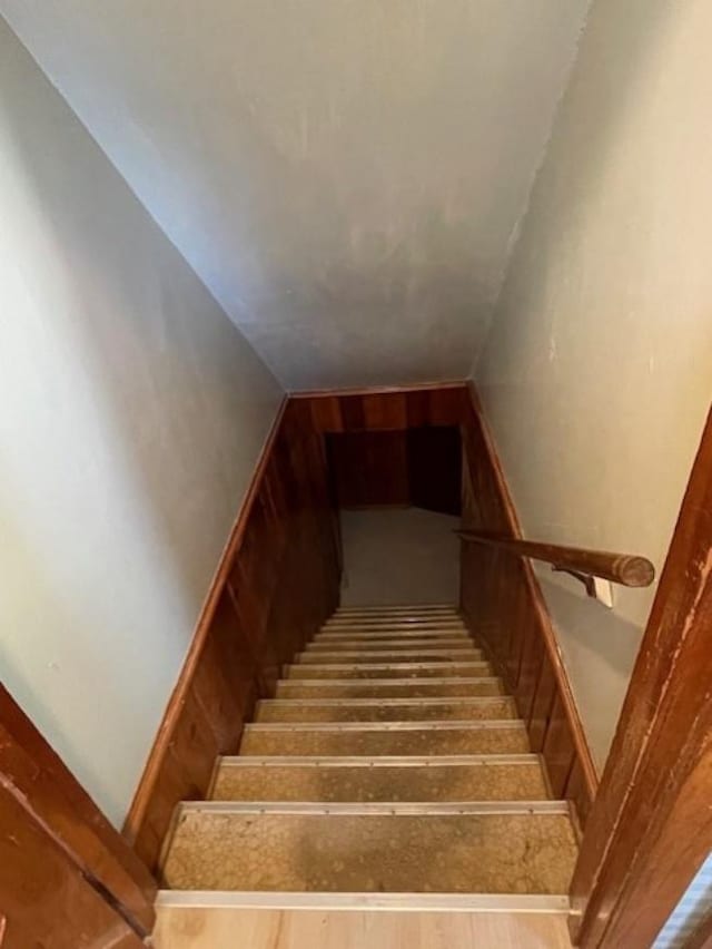 staircase with lofted ceiling, wood walls, and wood finished floors