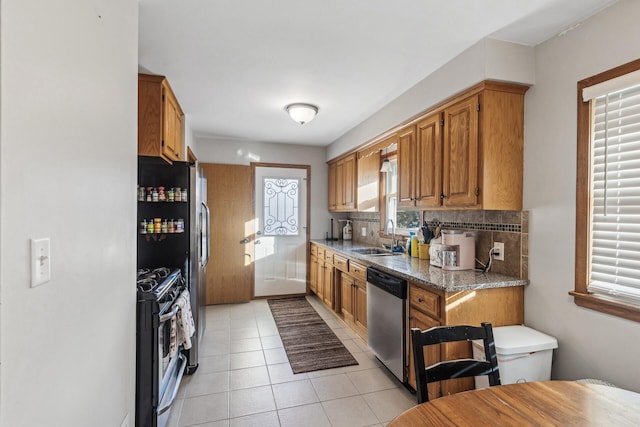 kitchen featuring sink, light tile patterned floors, dark stone countertops, stainless steel appliances, and tasteful backsplash