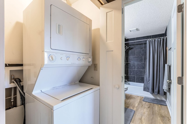 washroom with stacked washer and clothes dryer, light hardwood / wood-style floors, and a textured ceiling