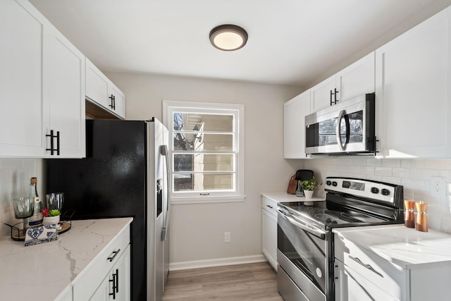 kitchen featuring white cabinetry, tasteful backsplash, stainless steel appliances, light stone countertops, and light hardwood / wood-style floors