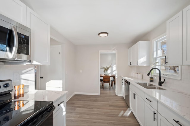 kitchen featuring sink, white cabinetry, light wood-type flooring, appliances with stainless steel finishes, and light stone countertops