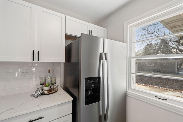 kitchen featuring white cabinets, tasteful backsplash, light stone countertops, and stainless steel fridge