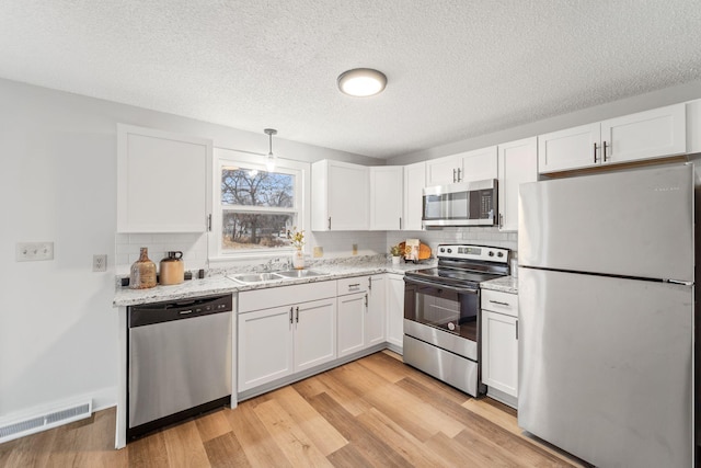 kitchen with sink, stainless steel appliances, white cabinets, and light wood-type flooring