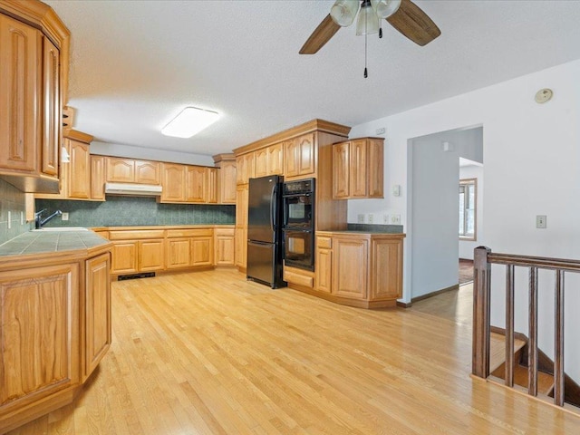 kitchen featuring black appliances, tile counters, ceiling fan, light hardwood / wood-style floors, and backsplash