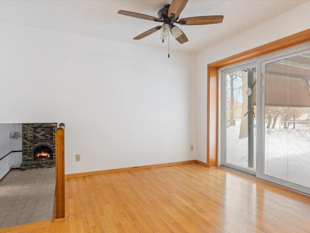 spare room featuring a brick fireplace, light hardwood / wood-style flooring, and ceiling fan