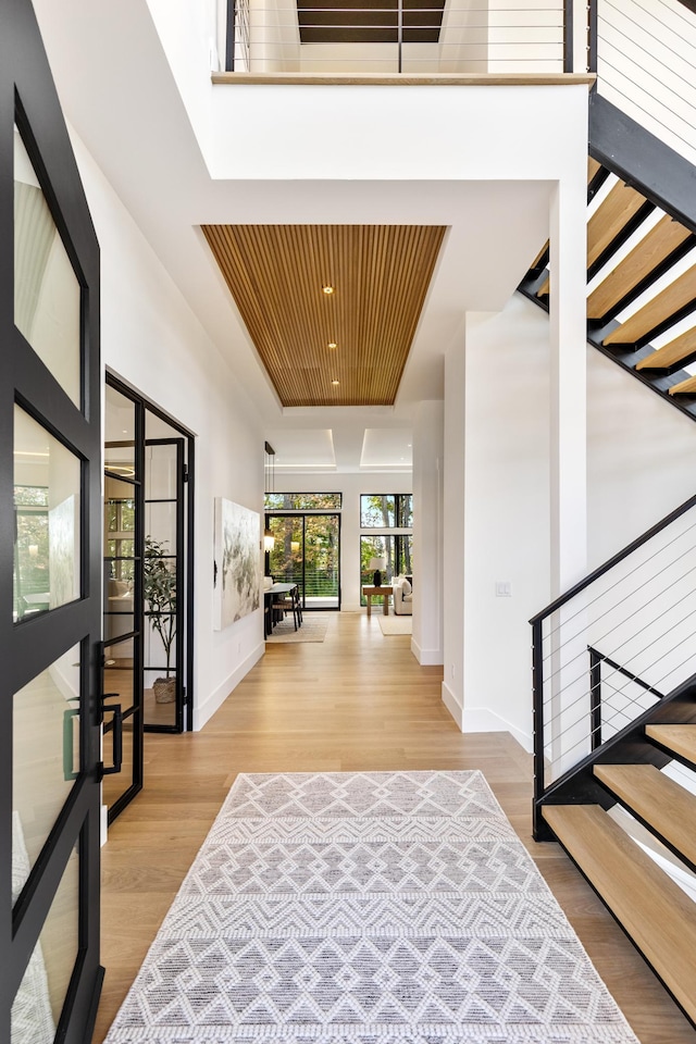 foyer with french doors, a raised ceiling, and light wood-type flooring