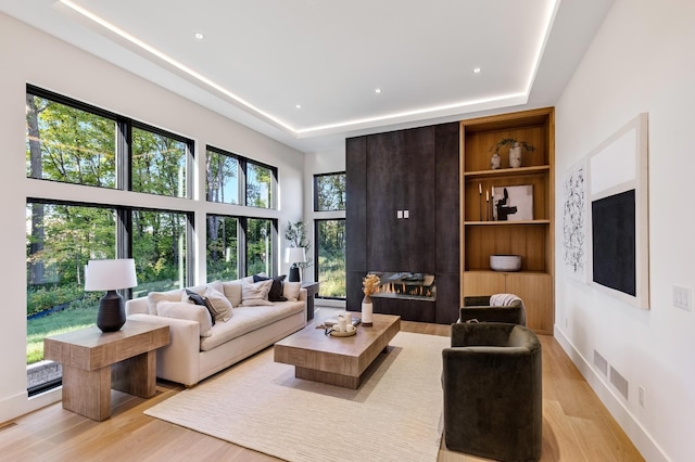 living room featuring a raised ceiling, built in features, and light hardwood / wood-style floors