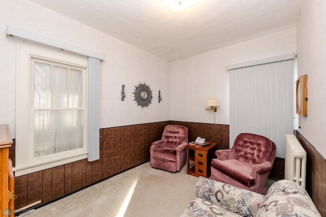 sitting room with radiator, wooden walls, and carpet flooring