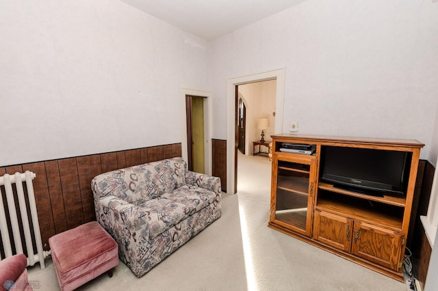 living area featuring carpet, radiator heating unit, and wood walls