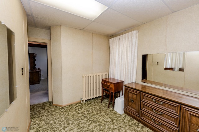 corridor with a drop ceiling, radiator heating unit, and light colored carpet