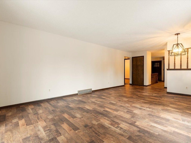 unfurnished living room featuring an inviting chandelier and dark hardwood / wood-style flooring