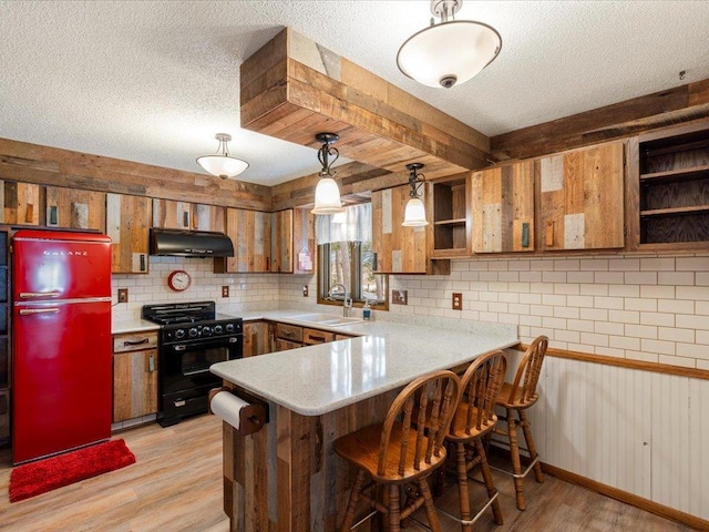 kitchen featuring sink, decorative light fixtures, refrigerator, kitchen peninsula, and black gas range