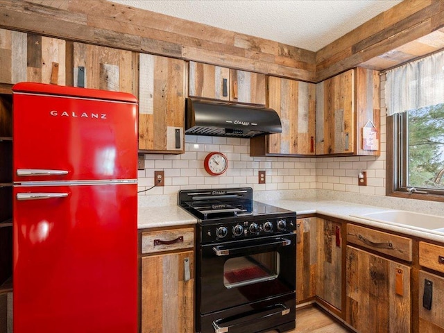 kitchen with sink, tasteful backsplash, refrigerator, a textured ceiling, and black range