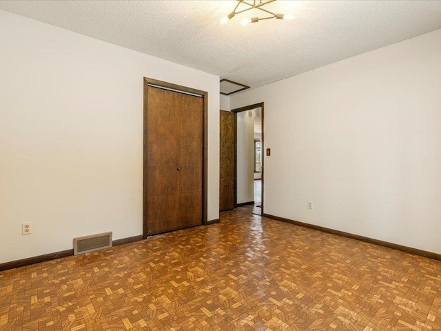 unfurnished bedroom featuring parquet floors, a notable chandelier, a closet, and a textured ceiling