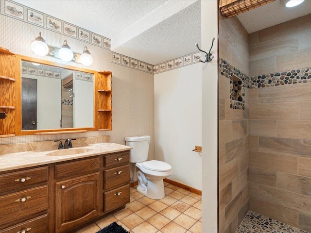 bathroom with tiled shower, toilet, a textured ceiling, vanity, and tile patterned flooring