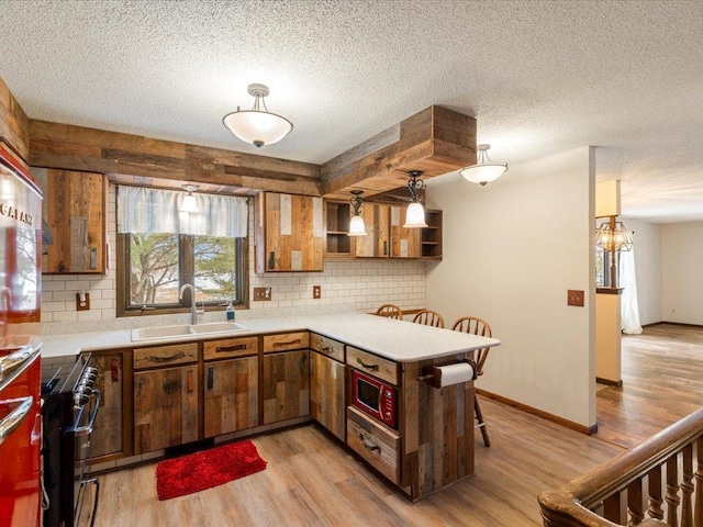 kitchen with sink, decorative light fixtures, light hardwood / wood-style flooring, and kitchen peninsula