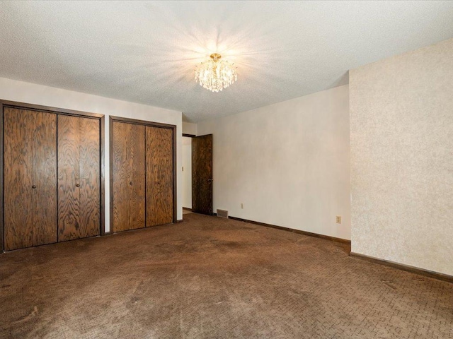 unfurnished bedroom with multiple closets, dark colored carpet, a textured ceiling, and an inviting chandelier