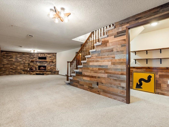 basement featuring wooden walls, a fireplace, carpet flooring, and a textured ceiling