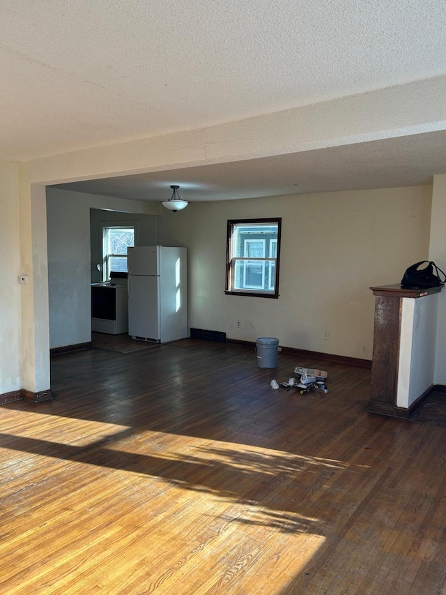 unfurnished living room with dark wood-type flooring, a healthy amount of sunlight, and a textured ceiling