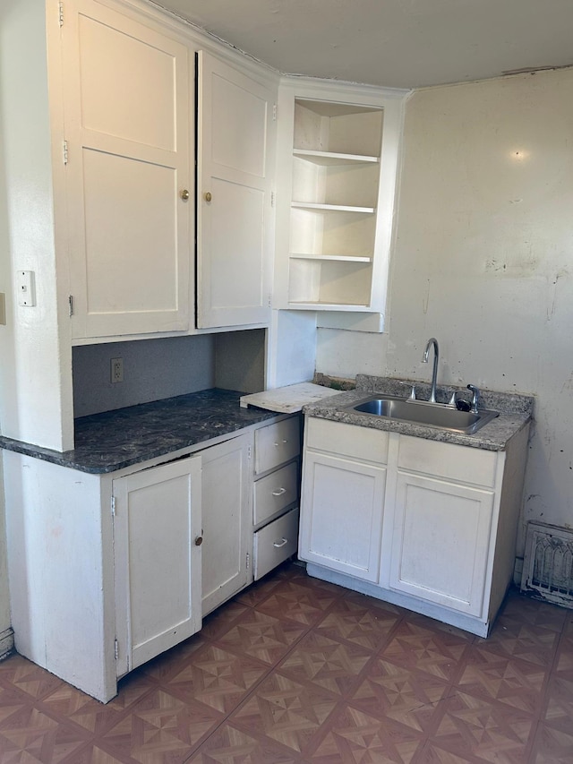 kitchen with dark parquet flooring, sink, and white cabinets