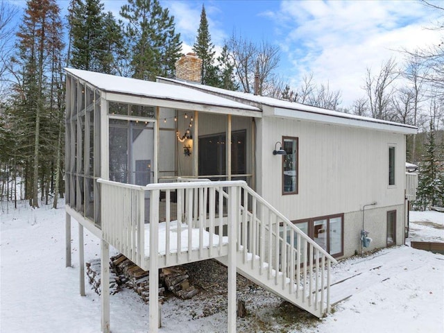 snow covered back of property with a wooden deck and a sunroom