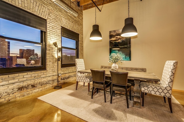 dining room featuring a towering ceiling, brick wall, and concrete floors