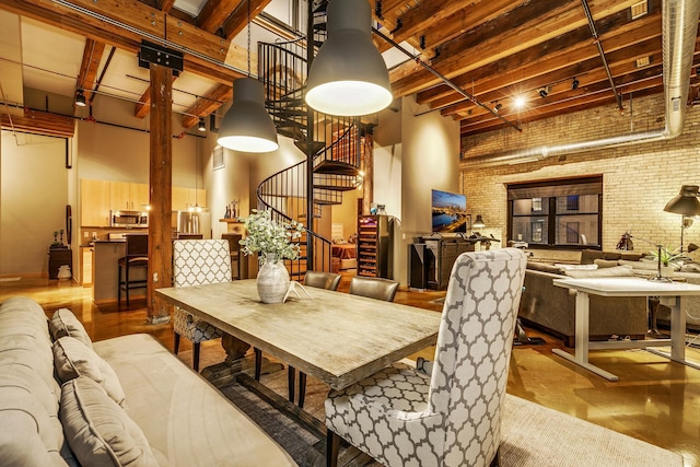 dining room with a towering ceiling, beamed ceiling, and brick wall