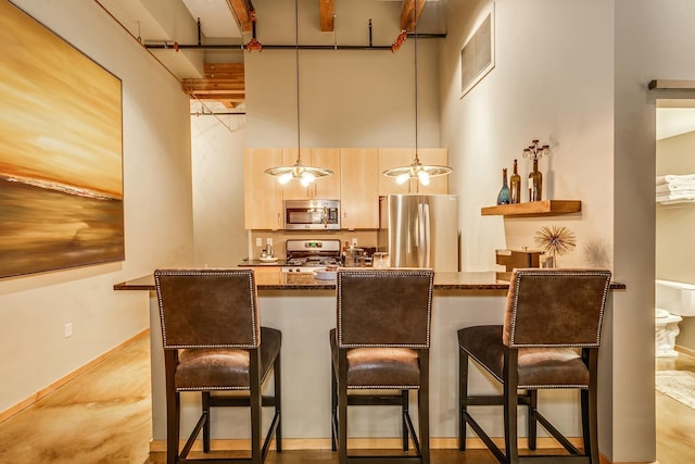 bar with light brown cabinetry, decorative light fixtures, dark stone counters, stainless steel appliances, and a high ceiling