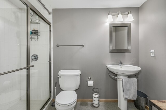 bathroom featuring toilet, sink, and a shower with shower door