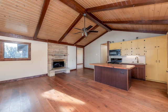 interior space featuring a fireplace, vaulted ceiling with beams, decorative backsplash, stove, and light wood-type flooring