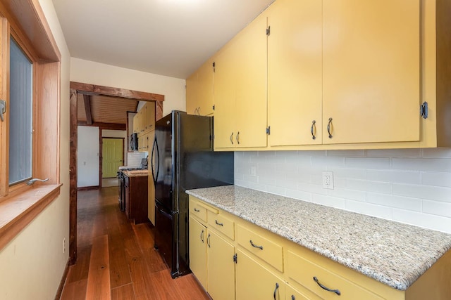 kitchen with dark wood-type flooring, black refrigerator, light stone countertops, range with gas stovetop, and decorative backsplash