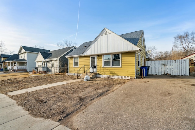 bungalow featuring roof with shingles, board and batten siding, and fence